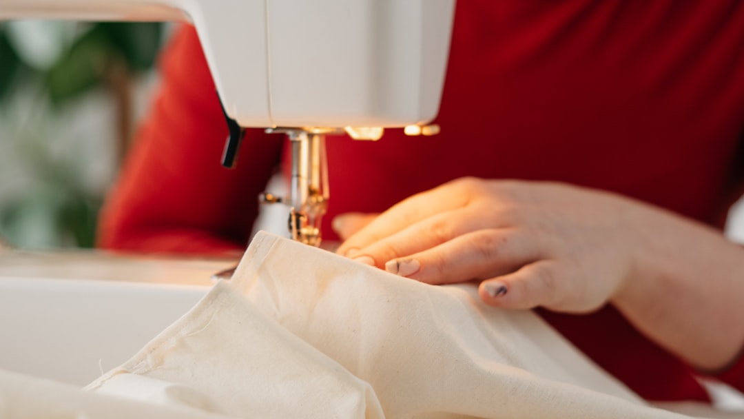 10 Essential Clothing Alterations Explained | Online Alterations & Tailor Guide 3 A woman's hand feeding white fabric through a sewing machine